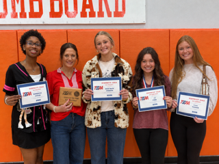 Four OCCHS Volleyball players and their coach smile in a group while holding certificates and a plaque.