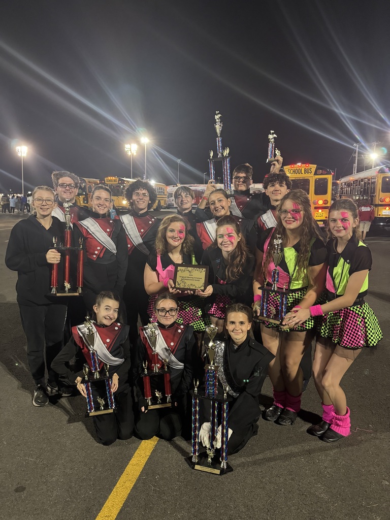 Members of the OCCHS marching band smile in a group while holding trophies.