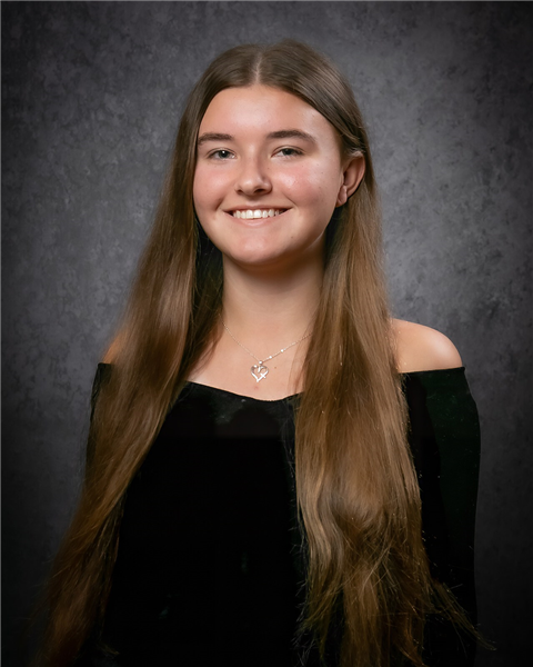 A girl student wearing a black drape smiles at the camera.
