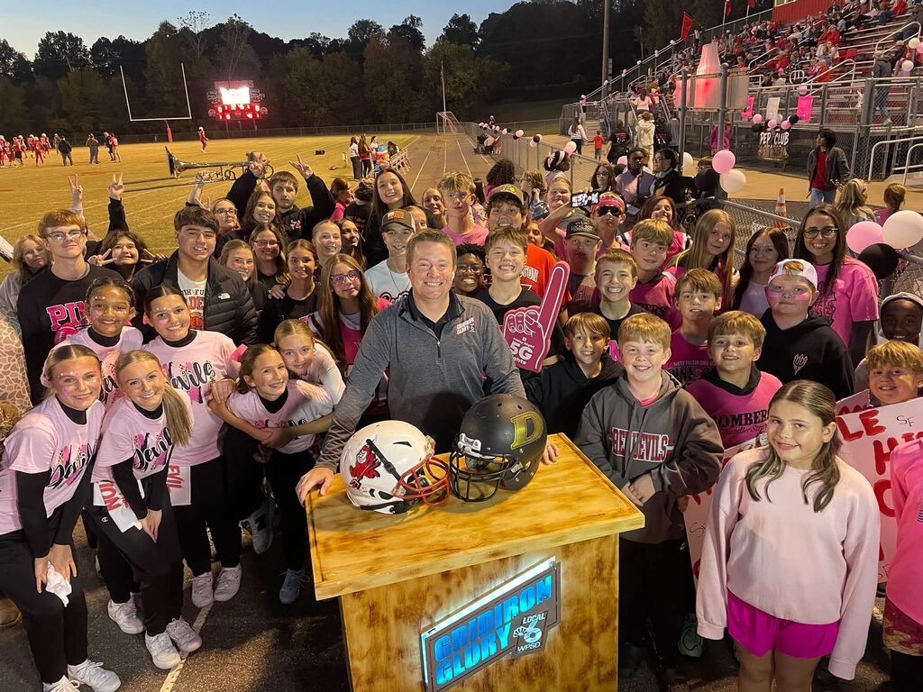 A group of South Fulton football supporters smile while surrounding a local news reporter.