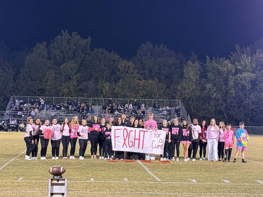 A group of South Fulton High School students gather on the football field holding a sign that reads "Fight for a cure".