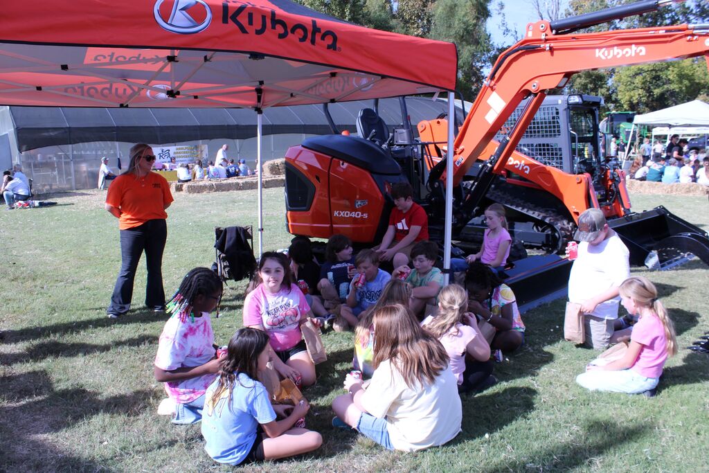 A group of students enjoy a snack while checking out large farm equipment.