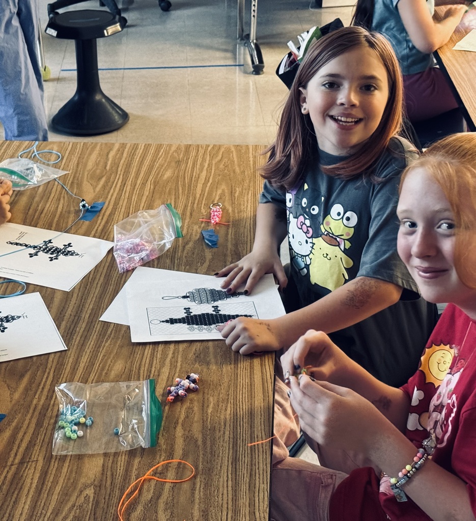 Two girls in a classroom putting together lizards made of pony beads