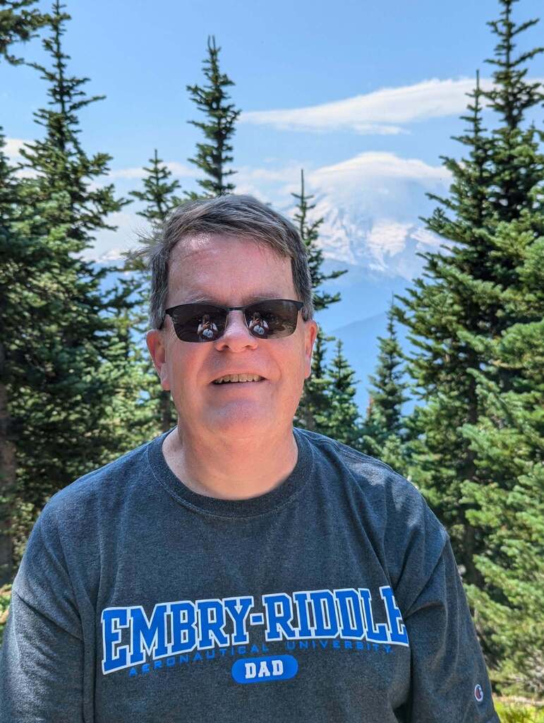 Don Ross standing in front of tree with a mountain in the background.