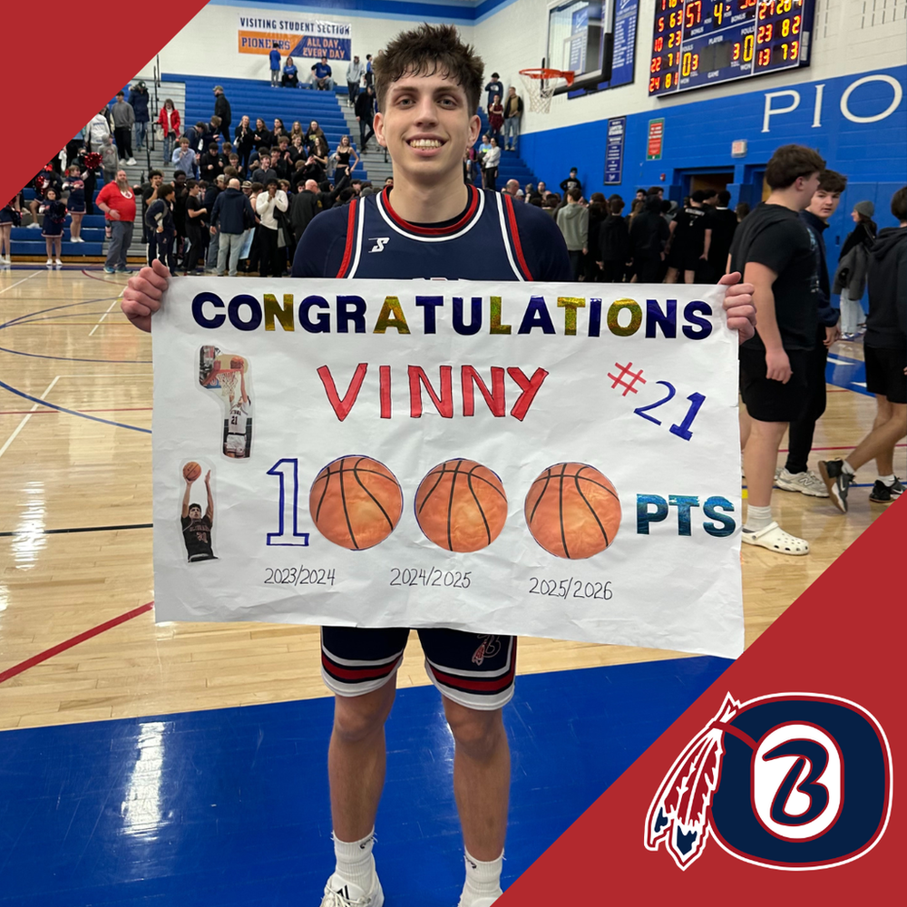 High school boys basketball player Vincent Thaler stands on the gym court holding a handmade sign that reads “Congratulations Vinny – 1,000 points,” celebrating his career scoring milestone, with teammates and fans in the background.