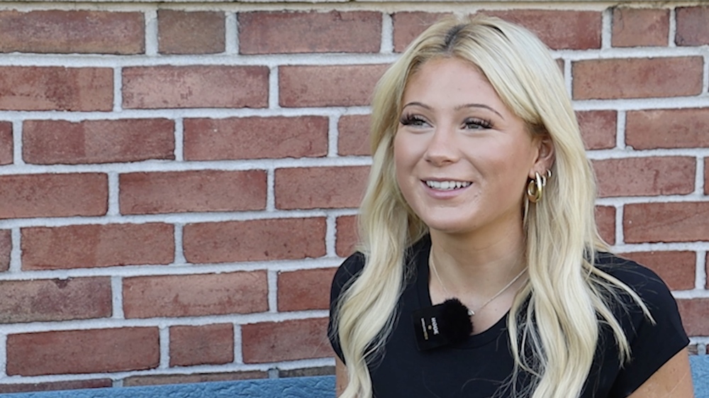 blonde student smiling in front of brick wall