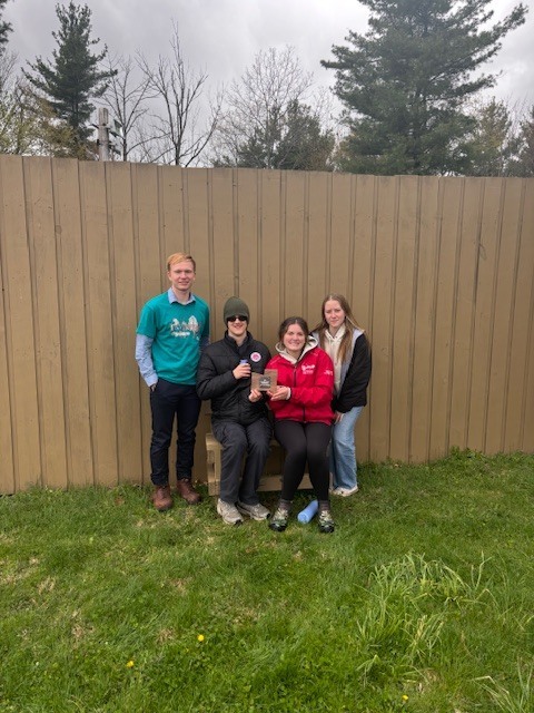 students posing in front of fence with award