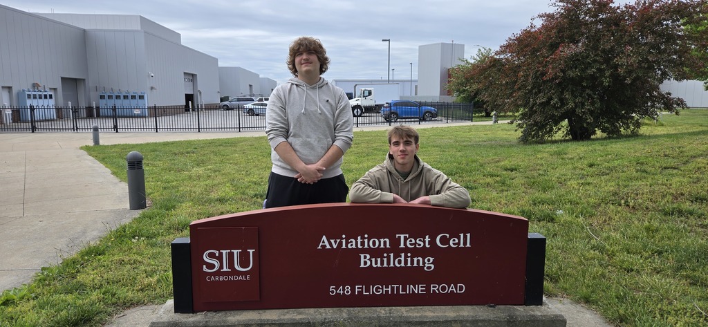 Two students who took the Part 107 drone exam standing behind the SIU-C School of Aviation Sign