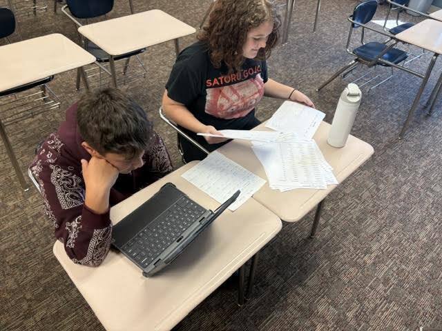 one student looking at computer,m one student looking at pile of papers