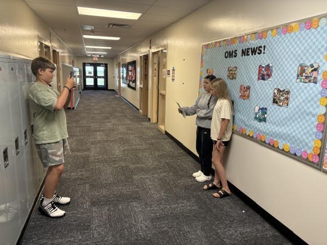 two students reading script in hallway while boy films with ipad
