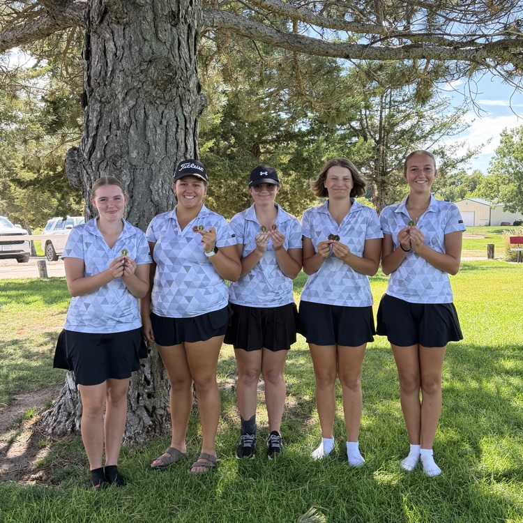 girls golf team in front of tree posing with medals