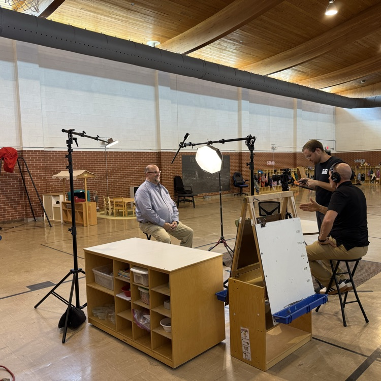 interview set up with two people setting up camera and man sitting on stopl