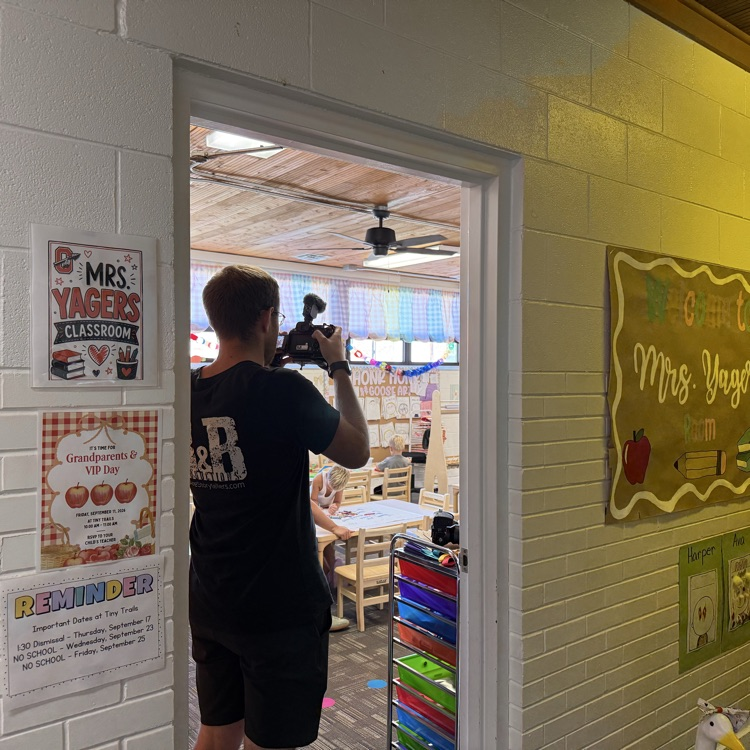 man taking video footage inside wide classroom door