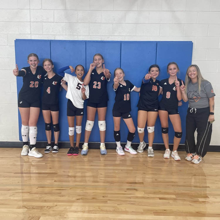 7th grade volleyball players standing in front of blue gym wall