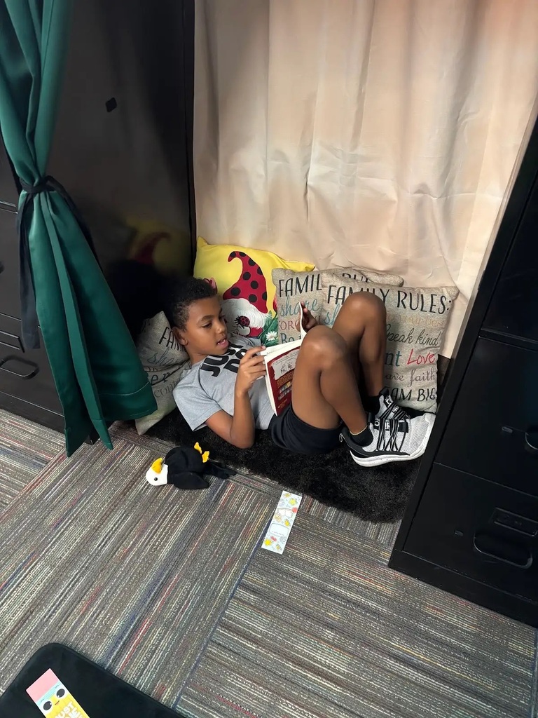 student laying in a cozy nook reading a book