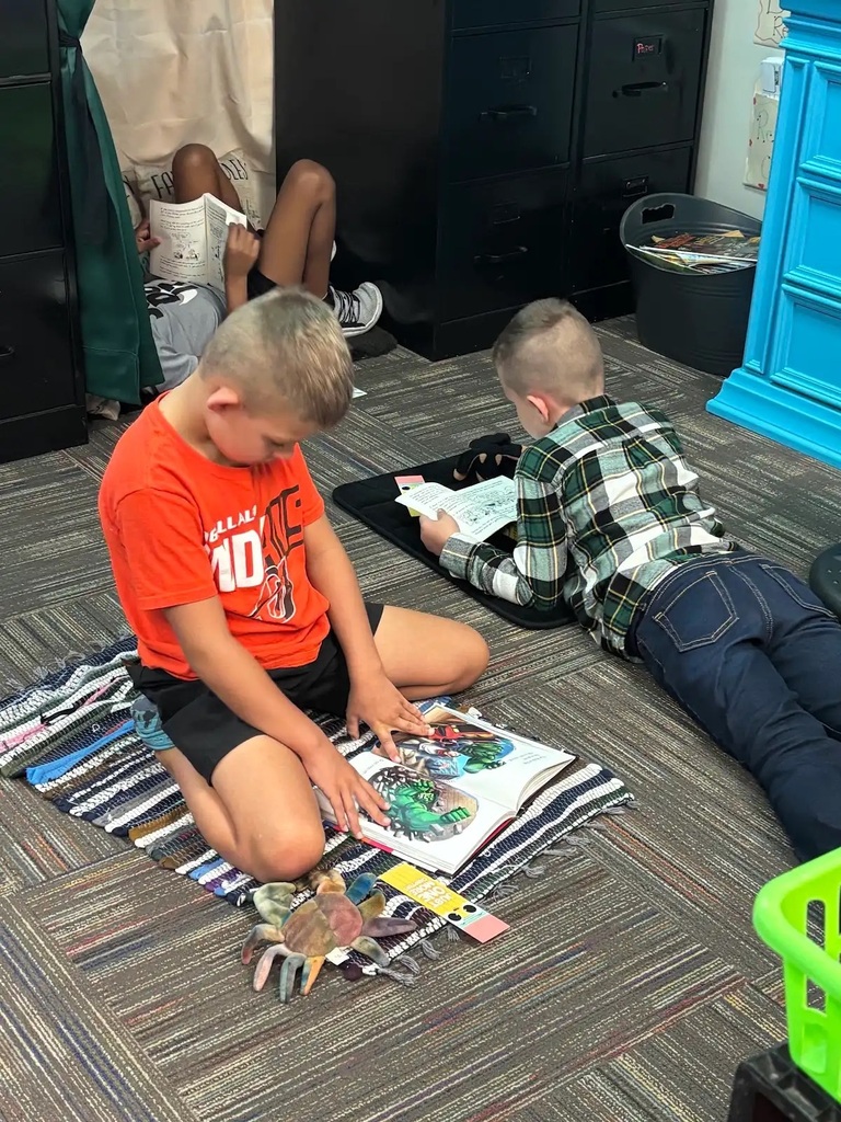 three students on rugs while reaidn gbooks and siting down