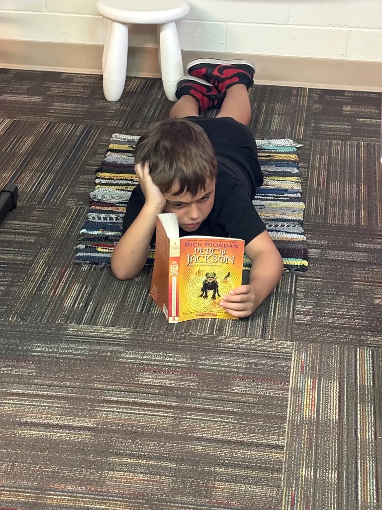 student laying on a rug holding up percy jackson book while reading