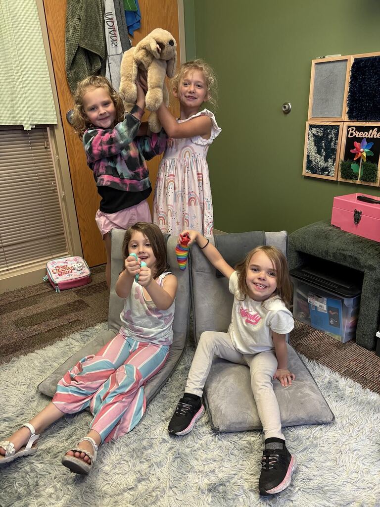 four girls holding up a dog. two girls are sitting on floor chairs, while two stand behind