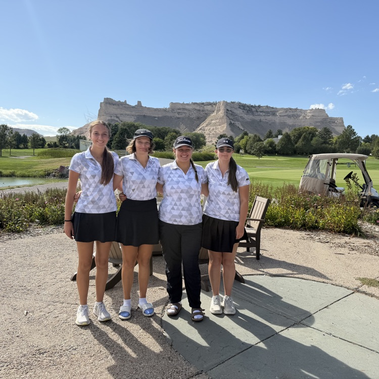 four golfers standing in front of Scottsbluff monument standing in a line
