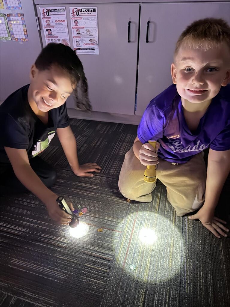 two boys shining flashlights at gems while smiling at cameras