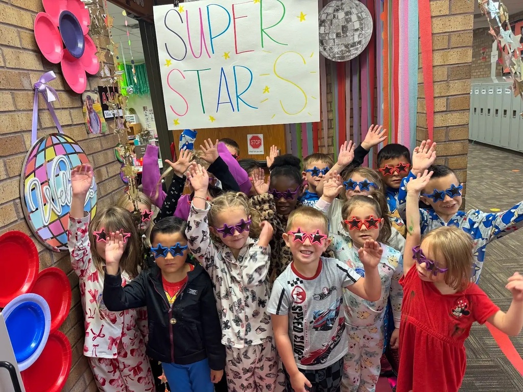 students with sunglasses on standing in front of a colorful sign that says super star s