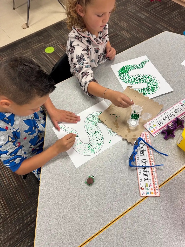 two students sitting at table making green dots in a snake outline