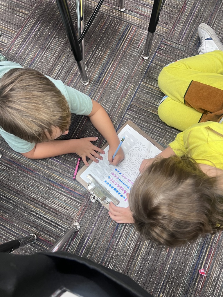 two students with a clipboard laying on the floor doing math