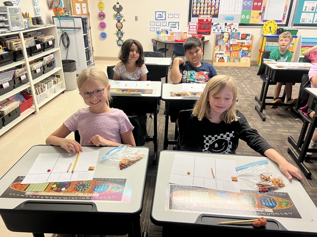 students sitting in desks in a classroom holding a bag of snacks smiling at the camera