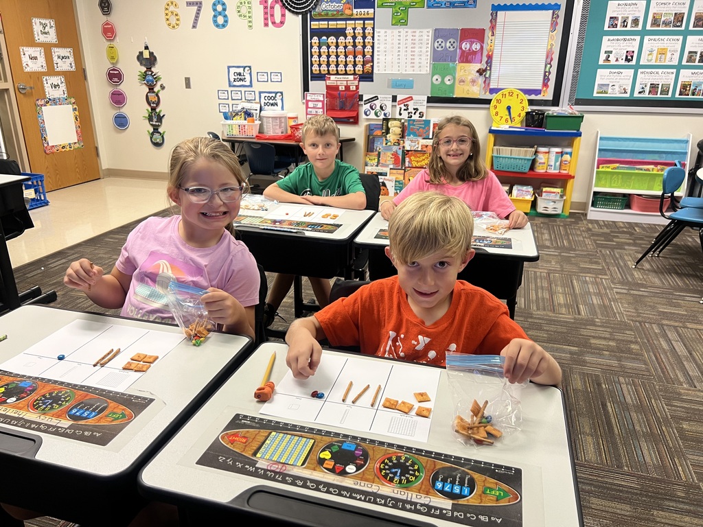 students sitting in desks in a classroom holding a bag of snacks smiling at the camera