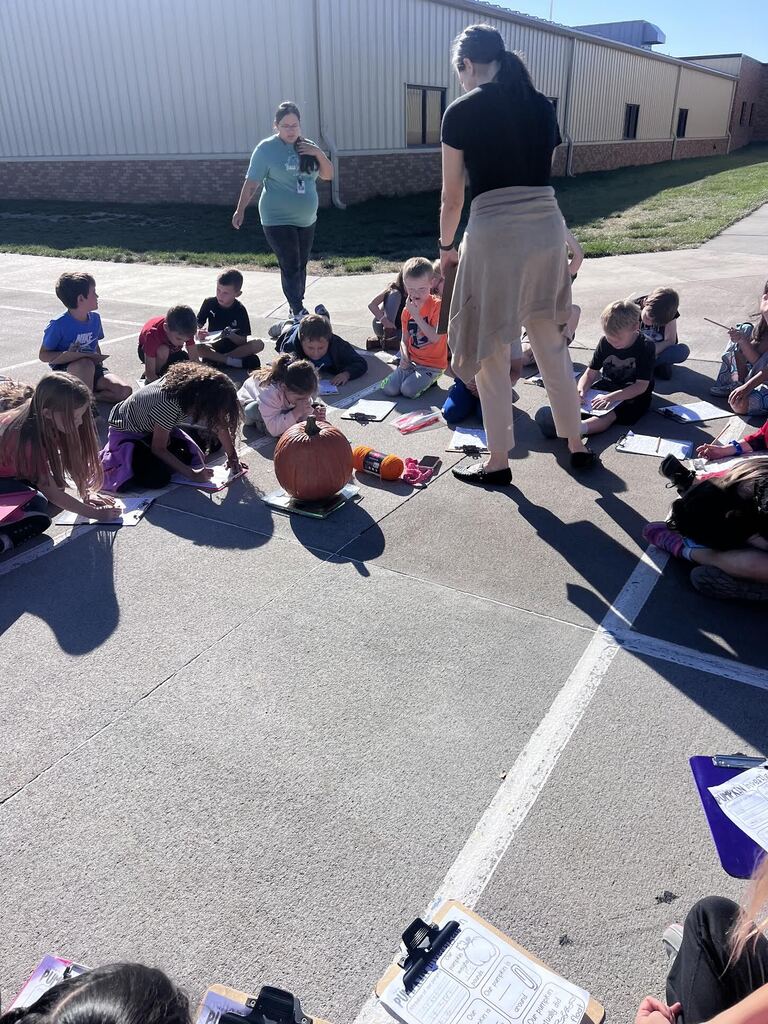 students sitting in a circle looking at pump;kin
