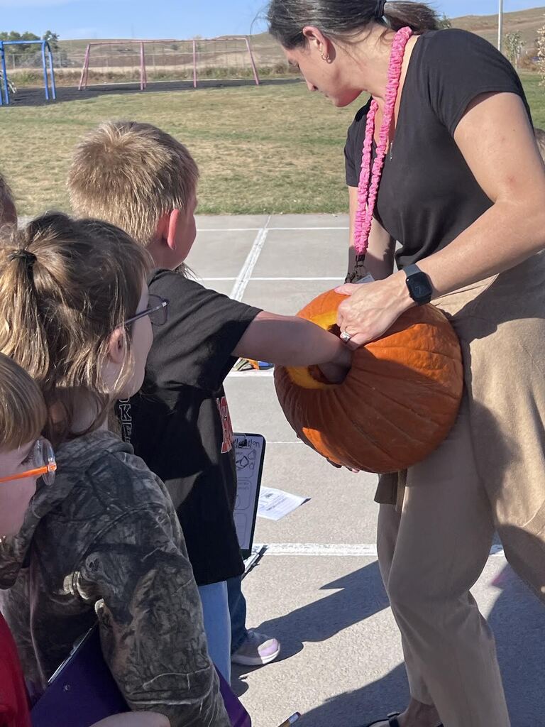 students putting hand inside of a pumpkin a teacher is holding