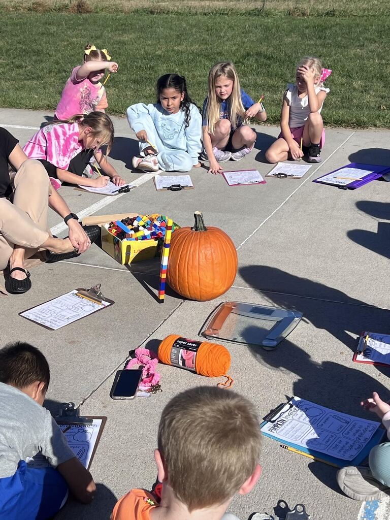 students sitting in a circle around a pumpkin measuring it with cubes