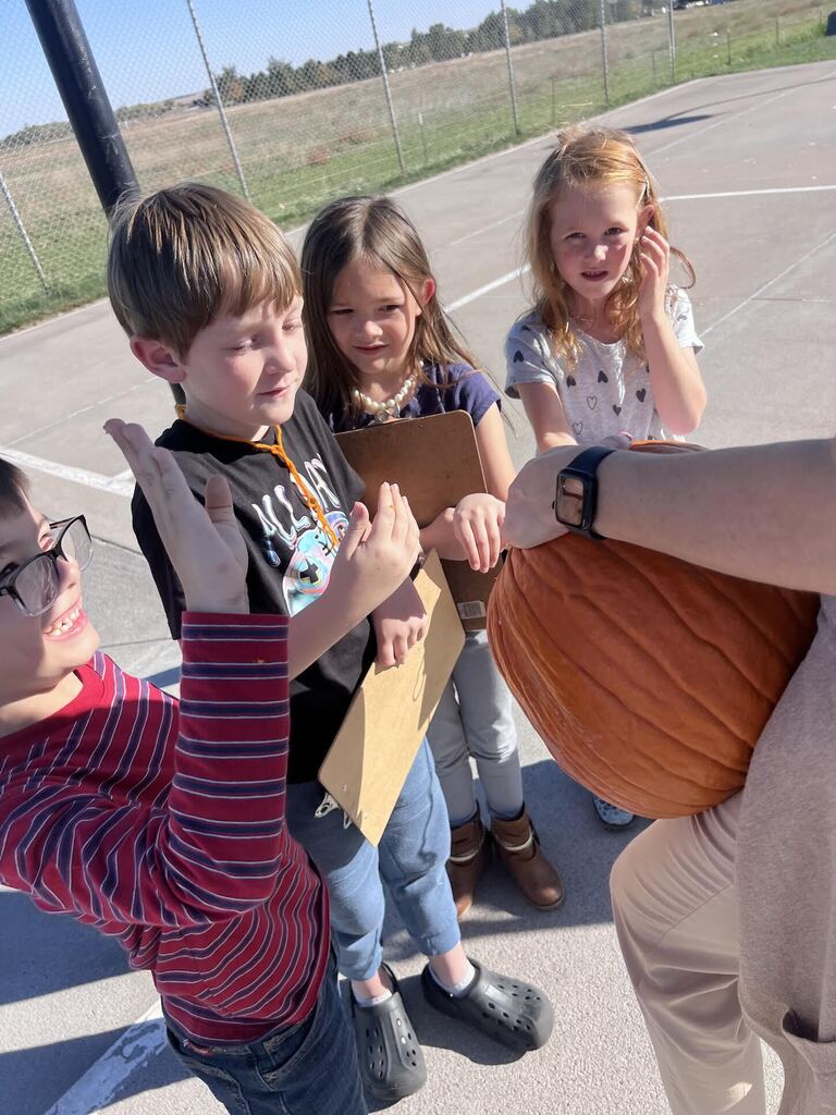 students putting their hand inside of a pumpkin a teacher is holding