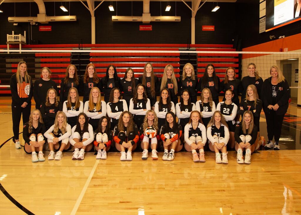volleyball team standing in front of net in 3 rows posing for picture