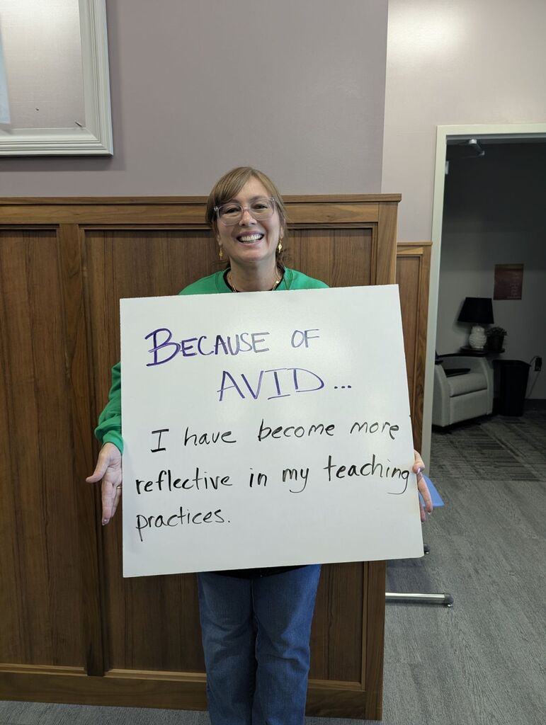 Teacher holding a white board explaining why they love AVID