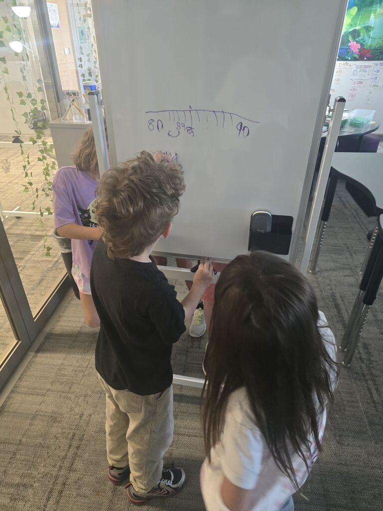 two students working together on a standing white board