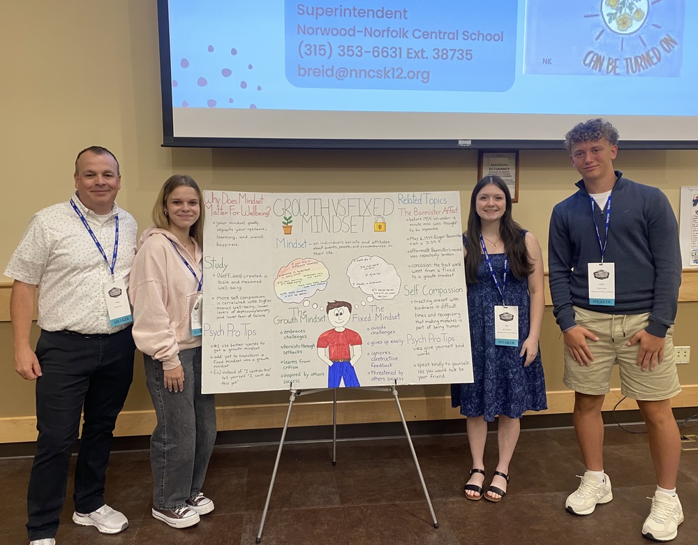 Photo of Ogdensburg Free Academy students Mia Jeneault, Jenna Pratt, and Urijah Austin along with social worker and instructor Mr. Greg Hooper presenting on The Science of Well-Being course in Lake Placid