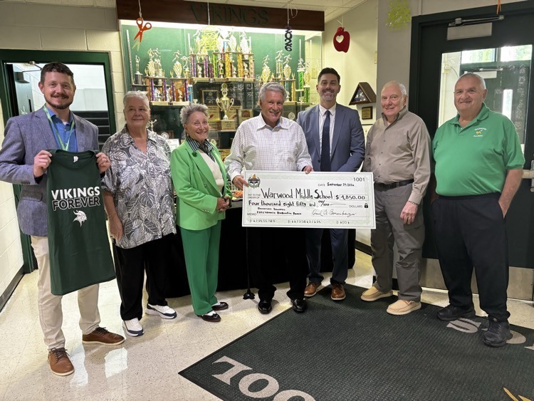 group of people smiling and standing with a large donation check