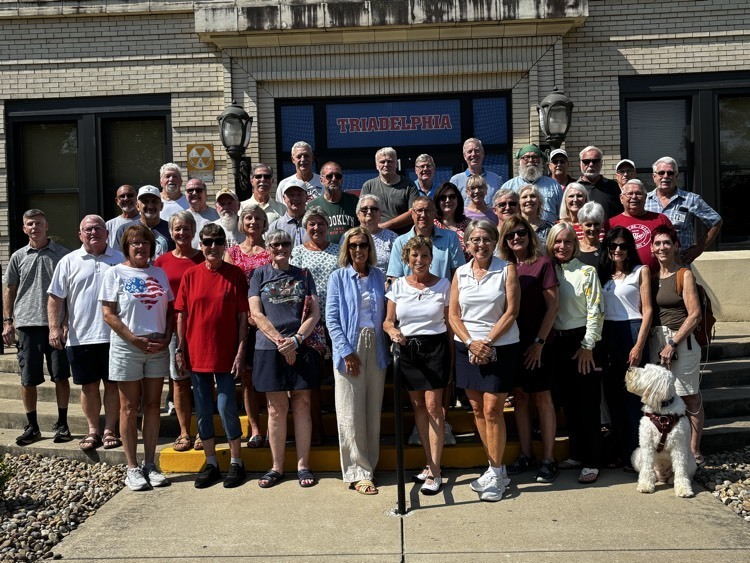 group of adults standing together smiling in front of a school 