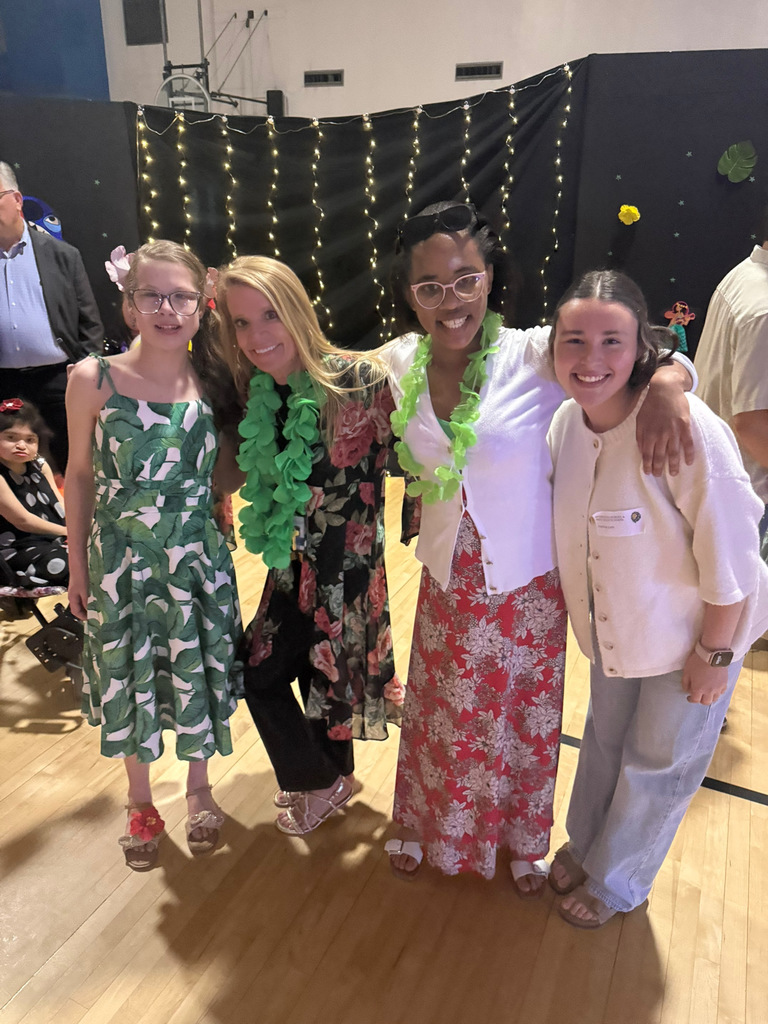 Assistant Principal Ms. Windham stands with students on a gymnasium floor in front of a decorated backdrop during a school prom.