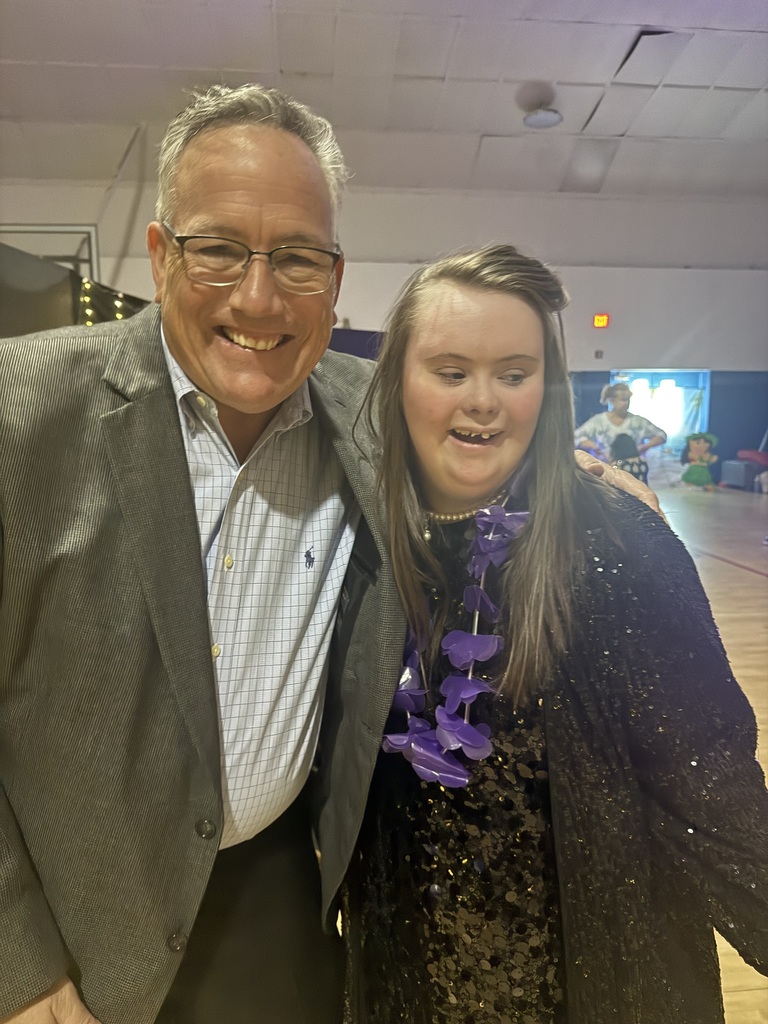 School Board member Mr. Tim Bryant poses with a student wearing formal prom attire in a school gymnasium during prom.