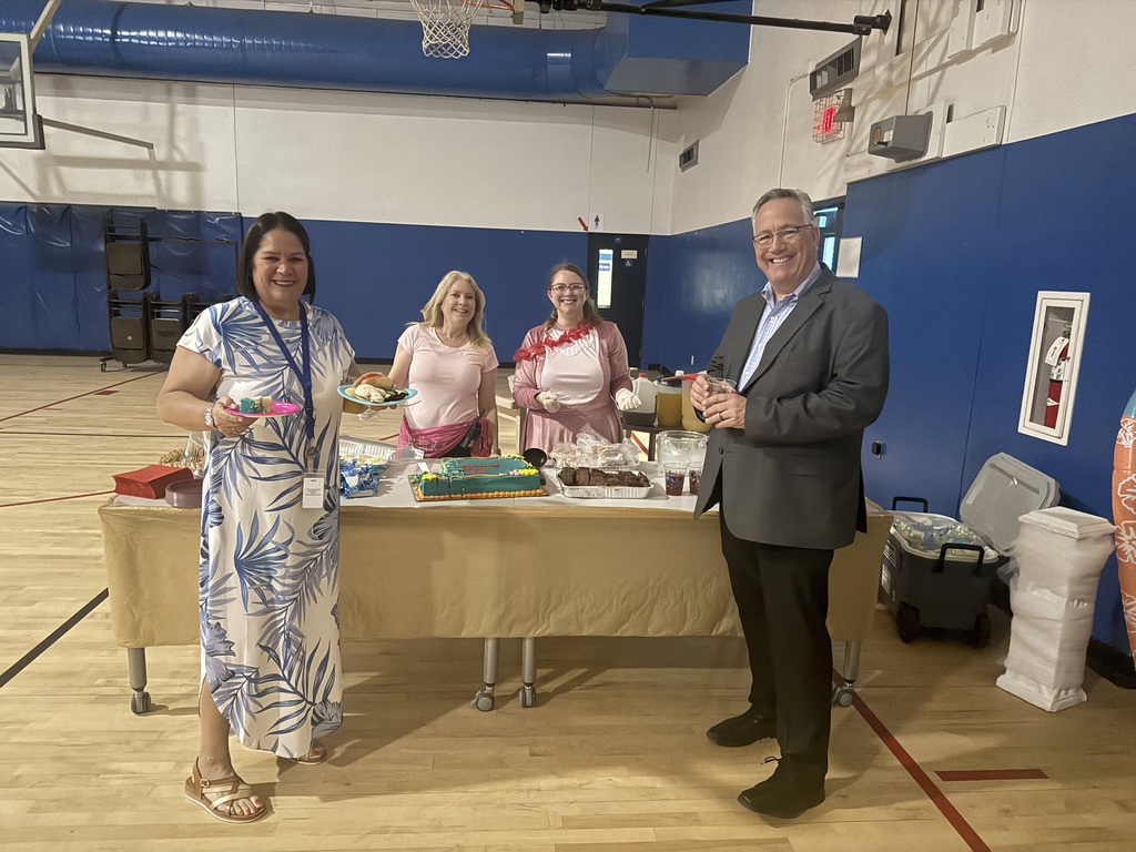 School Board member Mr. Tim Bryant stands with school staff members behind a refreshment table in a school gymnasium during prom.