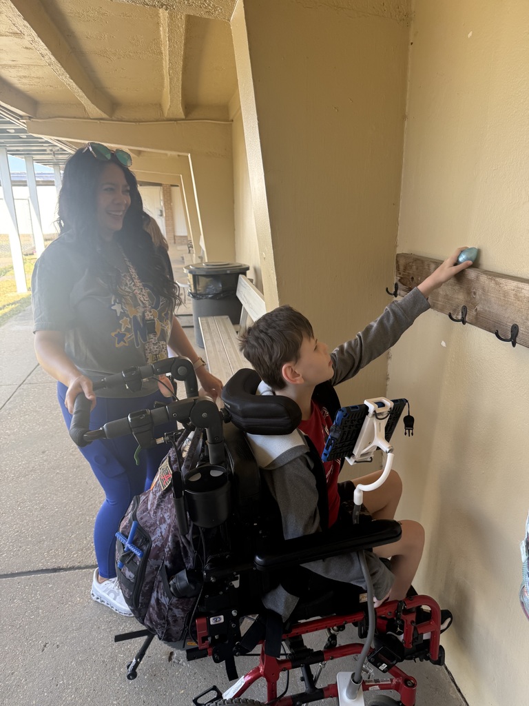 A student smiling while picking up a plastic egg during the school egg hunt, with a paraprofessional nearby smiling and observing.