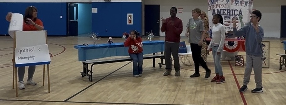 Students and staff participate in a patriotic skit during Richbourg School’s America250 celebration while standing in the gym decorated in red, white, and blue.
