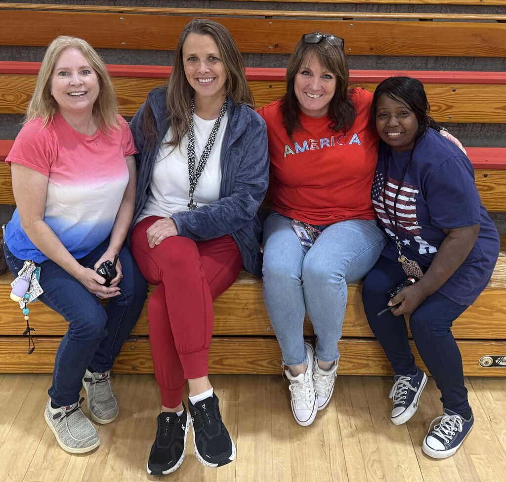 Four staff members wearing patriotic colors sit together in the gym during the celebration.