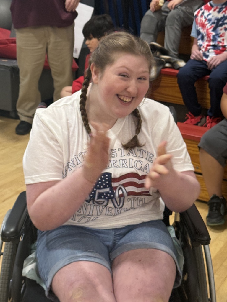 Student seated in a wheelchair smiles and claps during the patriotic celebration.