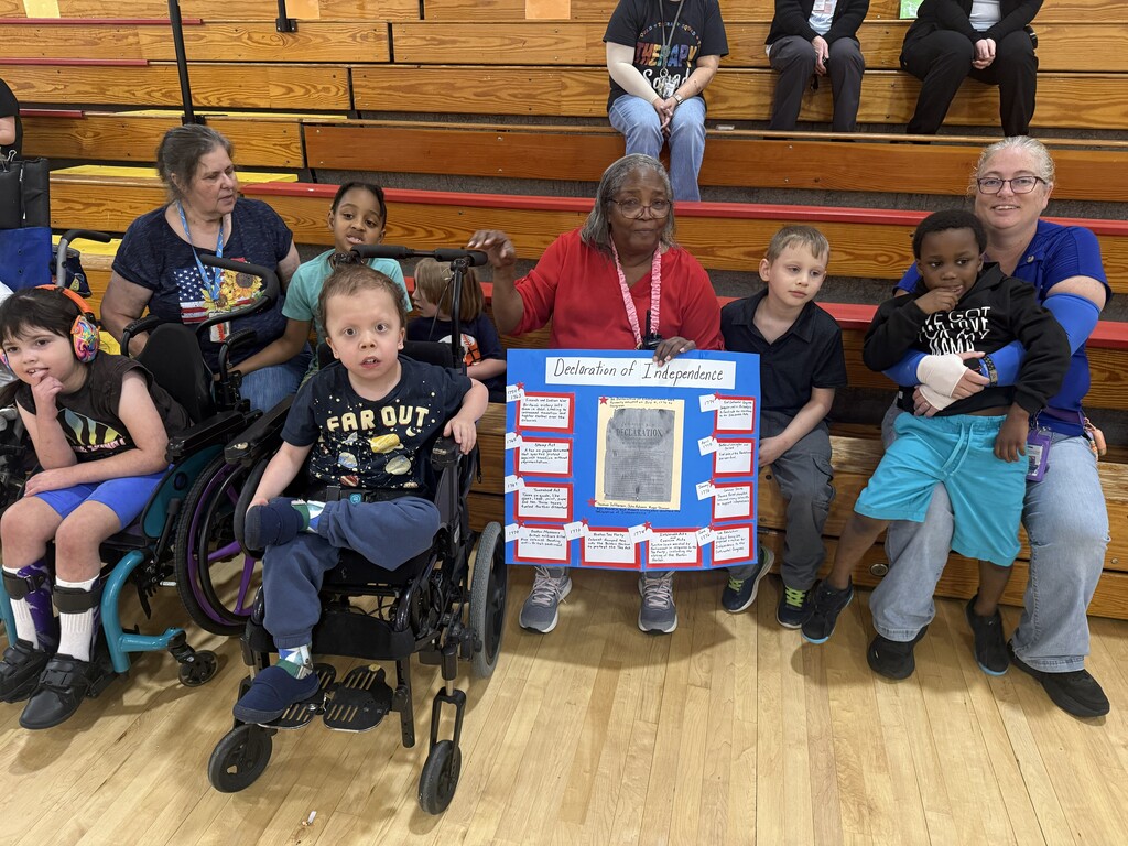 Students and staff pose together in the gym holding a Declaration of Independence poster display.