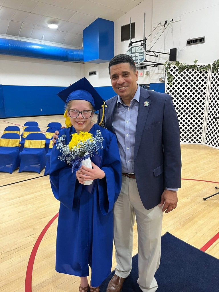 Superintendent Mr. Chambers poses with a Richbourg graduate in a blue cap and gown holding a bouquet of yellow and white flowers during the Class of 2026 graduation ceremony