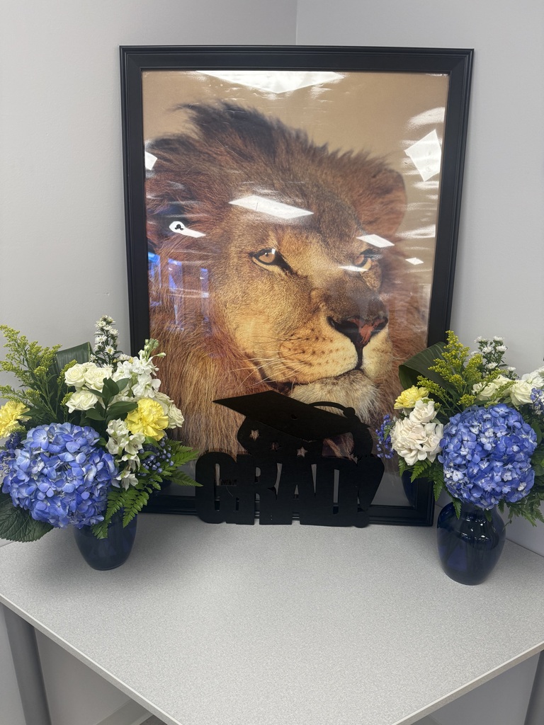 Framed lion artwork displayed with blue, white, and yellow floral arrangements created by The Pedal Barne in Crestview, along with graduation-themed decorations for the Richbourg Class of 2026 ceremony.