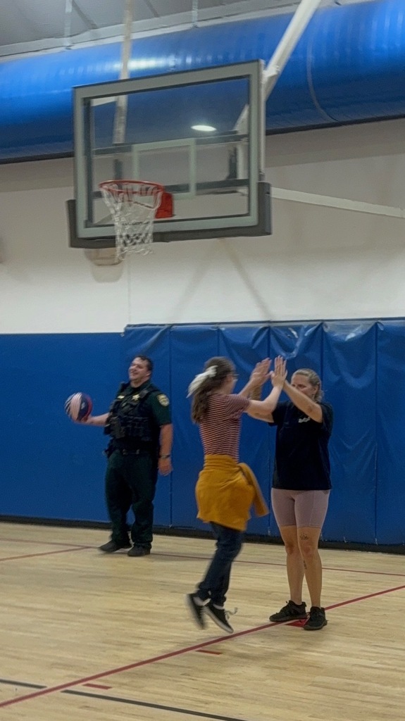 Two students celebrate with a high-five during the basketball game while a school resource officer stands nearby holding a basketball.